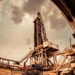 Oil drilling rig at dusk under a cloudy sky, representing the physical crude oil market behind WTI and Brent futures trading