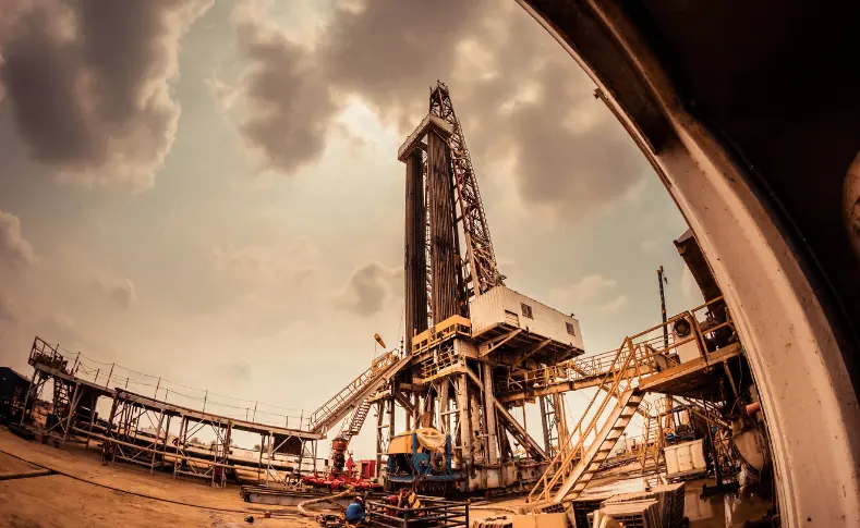 Oil drilling rig at dusk under a cloudy sky, representing the physical crude oil market behind WTI and Brent futures trading