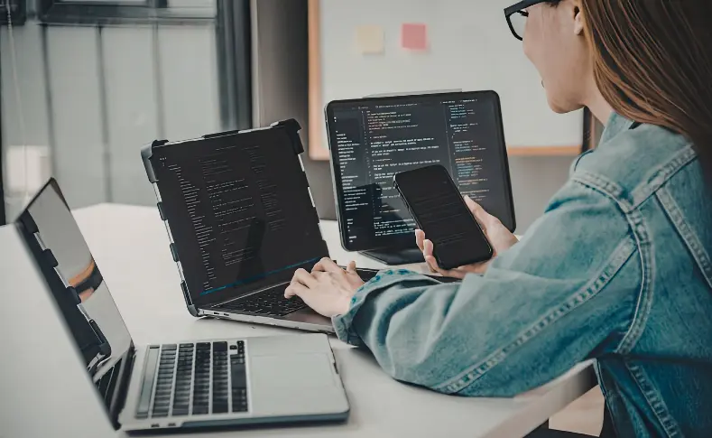 Person working across multiple laptops, a monitor, and a phone at once, representing how NTP keeps every connected device synchronized to the same time