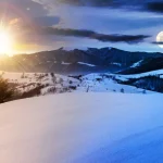 Sun and full moon visible together in the sky over a snow-covered mountain landscape, illustrating the seasonal shift in daylight through the year