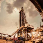 Oil drilling rig at dusk under a cloudy sky, representing the physical crude oil market behind WTI and Brent futures trading