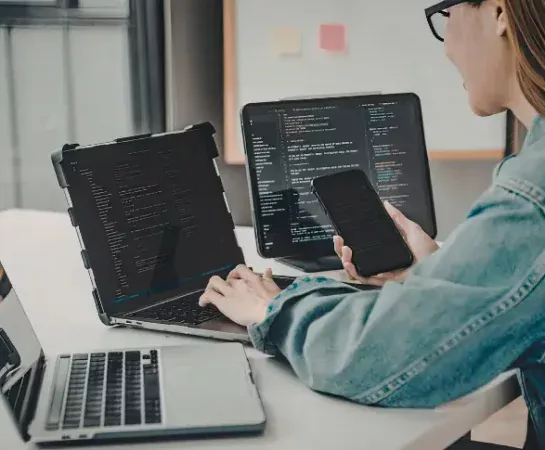 Person working across multiple laptops, a monitor, and a phone at once, representing how NTP keeps every connected device synchronized to the same time