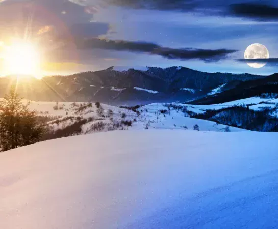 Sun and full moon visible together in the sky over a snow-covered mountain landscape, illustrating the seasonal shift in daylight through the year